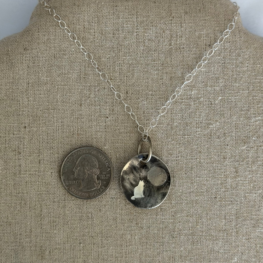 Cremation pendant in sterling silver is similar in size to a quarter.  There are ashes behind the moon.  Deep engraving of sitting cat shown.